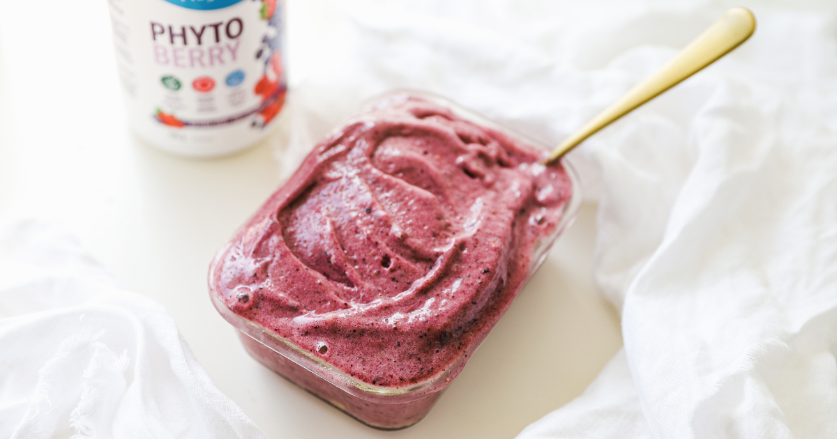 Berry vegan ice cream with a gold spoon on a white kitchen counter with Progressive PhytoBerry in the background