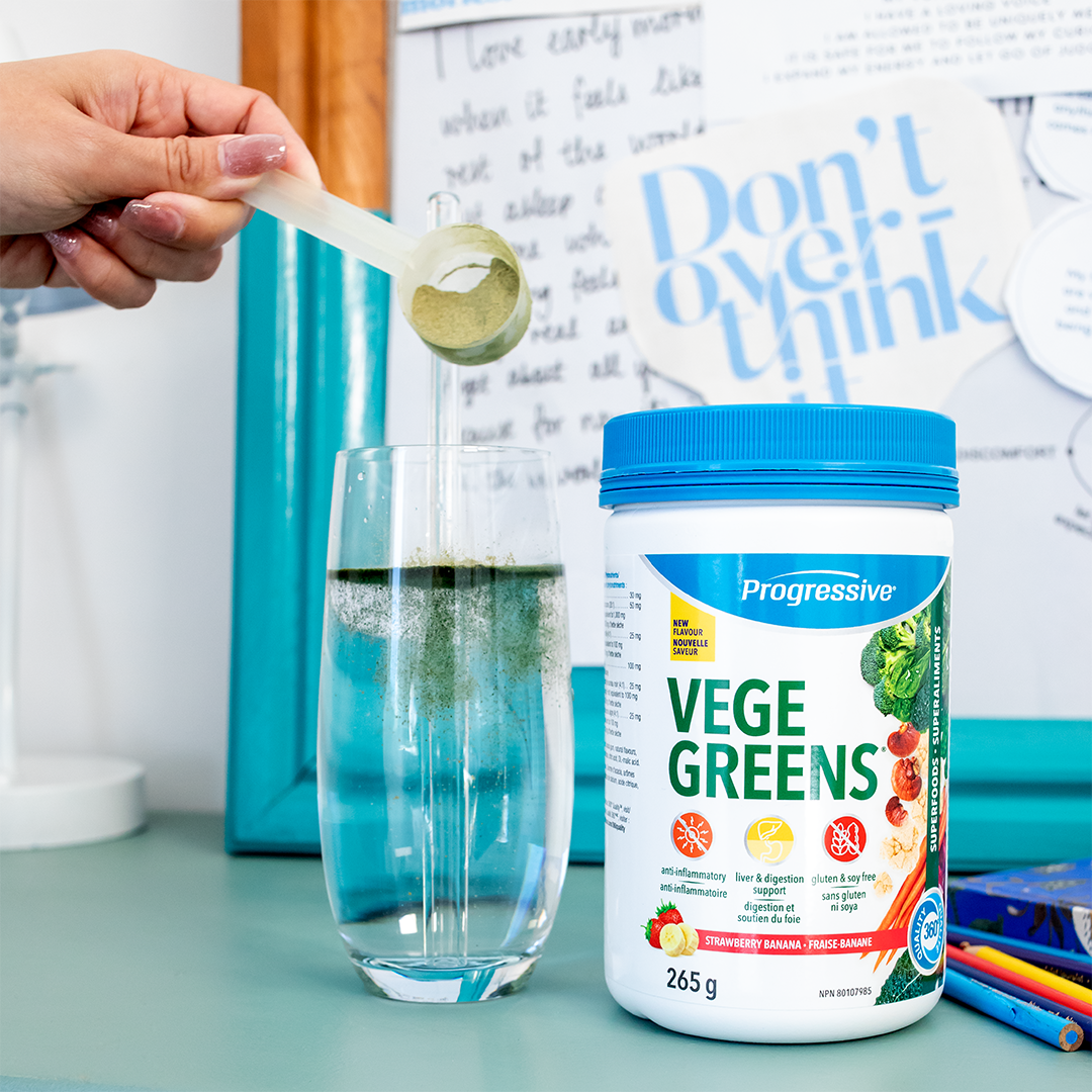 Person adding Vege Greens powder to a glass with a container of Progressive Vege Greens in the foreground.